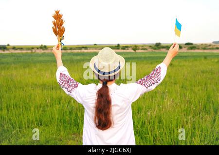 Unschärfe junge Frau in vyshywanka und Hut hält Bouquet von reifen goldenen Dornen von Weizen gebunden und Flagge auf der Wiese Natur Hintergrund. Flagge Ukrain Stockfoto