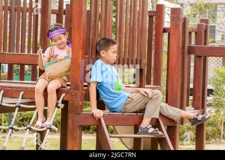 Ein Mädchen, das ein Märchenbuch für ihren Bruder auf der Treppe des Spielgrundes liest Stockfoto