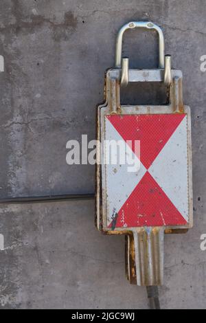 Nahaufnahme von Blechbahnsignalen mit roten weißen Dreiecken, die an Haken auf einem Betonsäulenhintergrund hängen Stockfoto