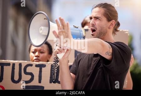 Der Anführer der Bewegung. Ein junger Mann mit erhobener Hand spricht durch ein Megaphon bei einem Protest. Stockfoto
