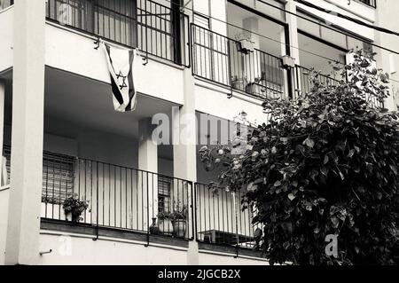 Israelische Flagge hängt vom Balkon eines typischen Gebäudes in Tel Aviv, Israel. Schwarzweiß-Foto. Stockfoto