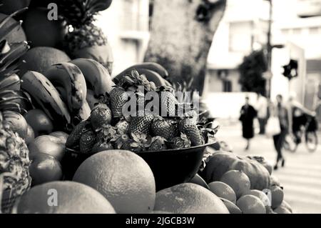 Tel Aviv, Israel. Obstsaftstand und Leute überqueren die Straße im Hintergrund. Urban Healthy Eating Konzept. Historisches Foto in Schwarzweiß Stockfoto