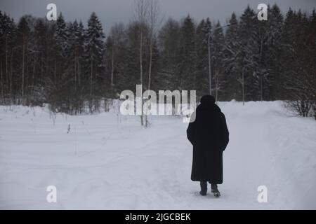 Sie ist im Winter auf der Straße im Mantel verheiratet. Rentner in Russland läuft durch den Park am verschneiten Tag. Mann in der Stadt. Graues Wetter. Stockfoto