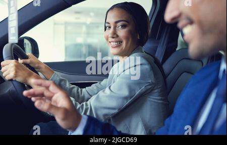 Es wird schwer sein, nein zu sagen... Ein beschnittenes Porträt einer attraktiven jungen Frau, die in einem neuen Auto sitzt, während sie mit einem hübschen männlichen Autoverkäufer spricht Stockfoto