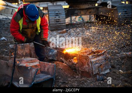 Ein Mitarbeiter im Helm schneidet alte Metallbalken für das Recycling vor Ort Stockfoto