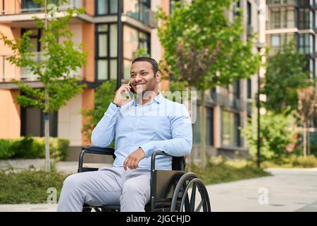 Fröhlicher, behinderter Mann, der sich am Handy unterhielt Stockfoto