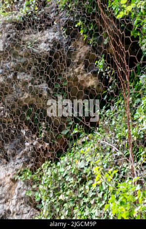 Ein schützendes Metallgeflecht schützt die Felsen vor Steinschlag. Metallisches Netz schützt die Straße vor Erdrutschen und fallenden Steinen. Sichere Bergausrüstung Stockfoto