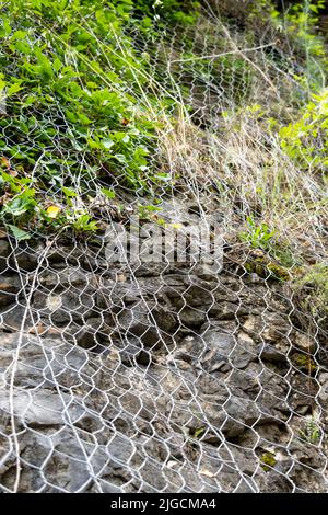 Ein schützendes Metallgeflecht schützt die Felsen vor Steinschlag. Metallisches Netz schützt die Straße vor Erdrutschen und fallenden Steinen. Sichere Bergausrüstung Stockfoto