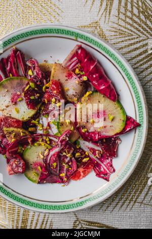 Radicchio Salat mit Wassermelone Rettich, Blutorange, Pistazien auf weißem Teller mit grünem griechischen Schlüssel Stockfoto