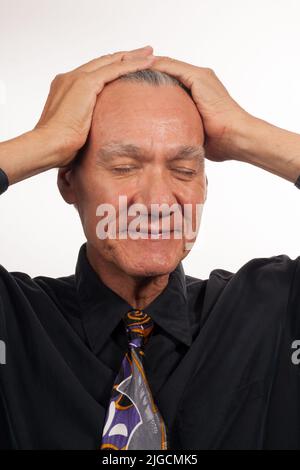 Reifer Mann in einem schwarzen Hemd und Krawatte mit den Händen auf dem Kopf Stockfoto
