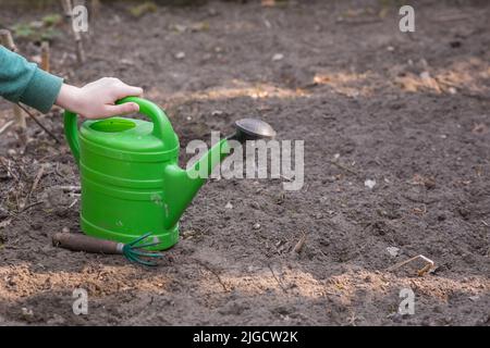 Die Hand der jungen Frau ist die grüne Gießkanne im Frühling Reinigung im Garten. Stockfoto