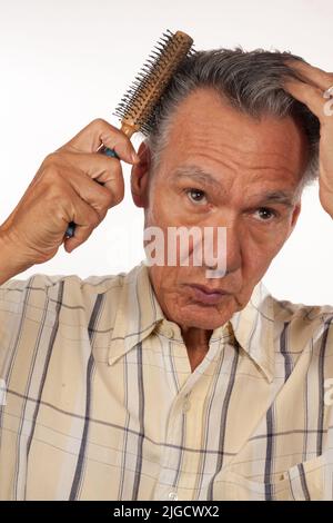 Reifer Mann 60 plus Kämmen seine Haare mit einem Pinsel Stockfoto