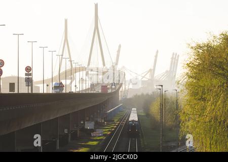 Kohlbrandbrücke in Hamburg Deutschland. Zug mit Container fährt unter. Schiffskrane im Hintergrund und Nebel Stockfoto