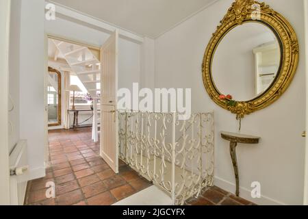 Retro-Schrank mit Dekorationen und Spiegel in der Nähe der Treppe und Tür zum Wohnzimmer im Flur des Hauses Stockfoto