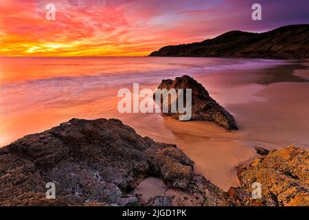 Strahlend heißer Sonnenaufgang über dem Pazifischen Ozean am Forster Town Burgess Beach mit malerischen Felsklippen und glattem Sand. Stockfoto