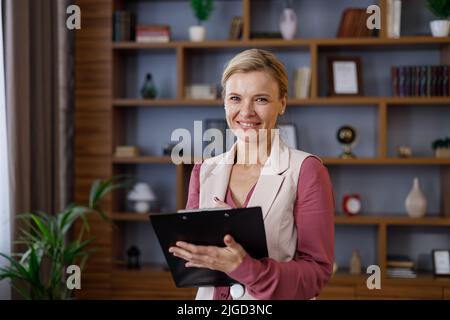 Portrait einer schönen lächelnden Psychologin, die Notizen auf der Zwischenablage gemacht hat. Professioneller Psychotherapeut, der im modernen Büro arbeitet. Stockfoto