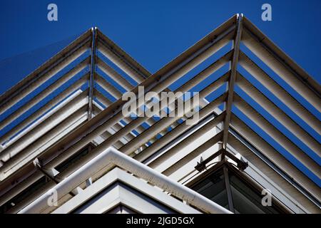 Abstrakte Ansicht von Sonnenschutzpaneelen, die dreieckige Linien auf der Seite eines Bürogebäudes schaffen Stockfoto