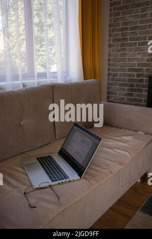 Geöffneter Laptop liegt am Arbeitstag mit einer Brille auf dem Sofa Stockfoto