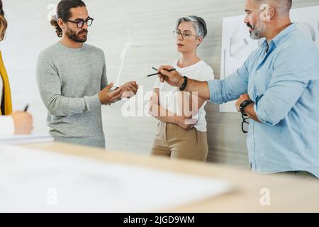 Eine Gruppe kreativer Designer, die während der Arbeit mit Modellen und Zeichnungen der Windturbine 3D eine Diskussion führen. Team aus innovativen Geschäftsleuten, die eine Stockfoto