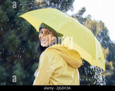 Ich hoffe, du bist von diesem Regen bedeckt. Eine Frau draußen im Regen mit einem gelben Regenmantel und einem Regenschirm. Stockfoto