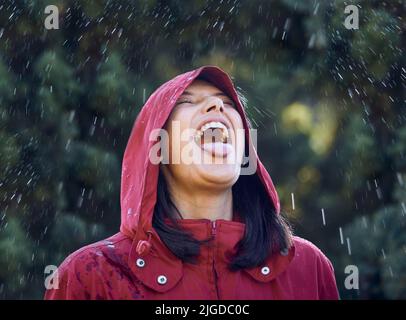 Ohne Regen gibt es keine Regenbögen. Eine junge Frau ragt aus ihrer Zunge, um den Regen draußen zu spüren. Stockfoto