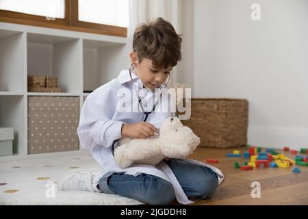 Engagierter Junge im medizinischen weißen Mantel, der die Rolle des Arztes spielt Stockfoto