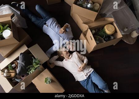 Glückliches Paar neuer Hausbesitzer, die sich auf dem Boden zwischen den Boxen ausruhen Stockfoto