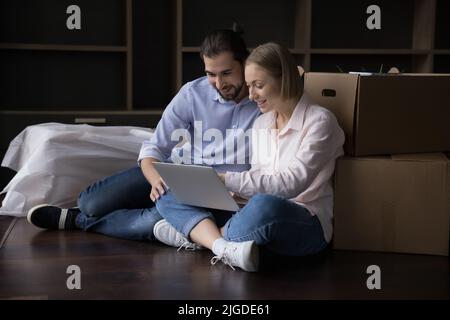 Ein glückliches Paar von Hausbesitzern, die auf einem Haufen von Boxen einen Laptop benutzen Stockfoto