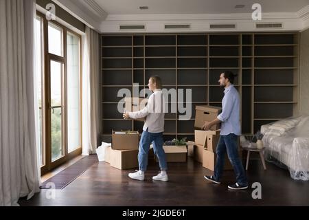 Junges, tausendjähriges Ehepaar, das Kisten in ein leeres Wohnzimmer trug Stockfoto