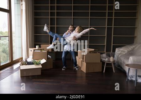 Glücklicher Hausbesitzer Kerl trägt Freundin in Armen im Wohnzimmer Stockfoto
