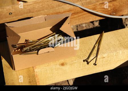 Ein offener Schraubkasten liegt auf einem Holzbalken. Reparatur des Decks. Stockfoto