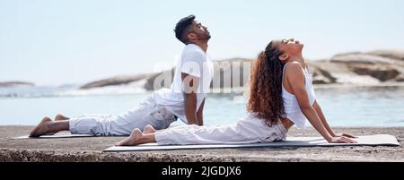 Gut für Geist, Körper und Seele. Ganzkörperaufnahme eines jungen Paares, das am Strand Yoga praktiziert. Stockfoto