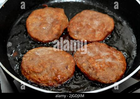 Fleischburger, die auf flachem Öl auf einer Bratpfanne gebraten werden, Hackfleischpastete in Form von Hackfleisch, und es ist ein beliebter schneller Schrott Stockfoto