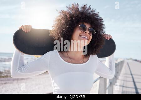 Lassen Sie die guten Zeiten Rollen. Eine junge Frau hängt mit ihrem Skateboard an der Promenade. Stockfoto