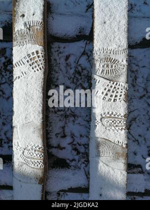 Menschliche Fußabdrücke auf dem Schnee. Zwei Holzplanken sind mit Schnee- und Schuhsohlendrucken bedeckt. Stockfoto