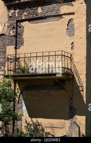 Altes Gebäude mit einem blinden, gemauerten Balkon ohne Eingang und einer alten Fassade mit abblätterndem Putz. Stockfoto