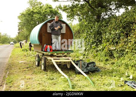 Ein junger Mann mit seinem Zigeunerwagen, der am Rande der Appleby Horse Fair in Appleby in Westmorland, Cumbria, campt Stockfoto