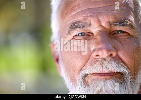 Die Augen haben immer eine Geschichte zu erzählen. Ein älterer Mann schaut während eines Tages im Park in die Kamera. Stockfoto