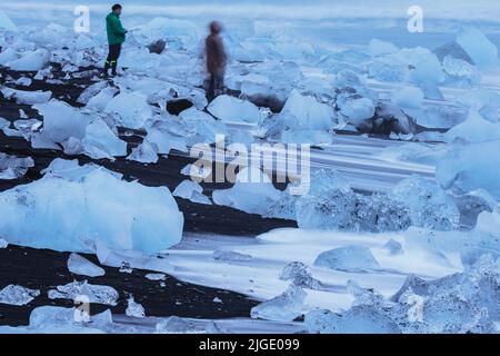 Verschwommene Touristen, die Fotos über dem schwarzen Sandstrand machen, Langzeitbelichtung Stockfoto