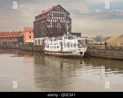 Klaipeda, Litauen - April 2018: Altes Boot auf dem Fluss Danė. Im Hintergrund das Old Mill Hotel. Dane River, Osteuropa. Stockfoto