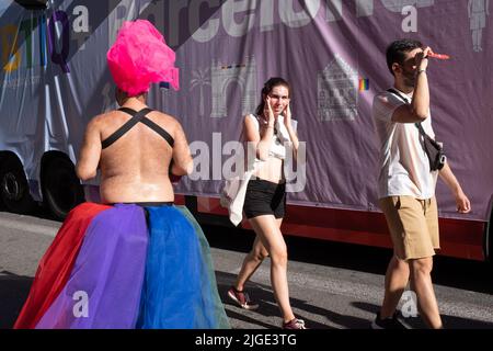 Barcelona, Spanien - 25. Juni 2022:Gay Pride 2022. Rückansicht eines Nachtschwärmers mit einem bizarren Kopfschmuck und zwei Touristen, die in die entgegengesetzte Richtung gehen Stockfoto