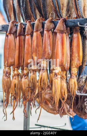 Rauchgetrocknete Calamari oder Tintenfische auf einem Fischmarkt hängen, die gerade mit Holzschnitzeln in einem Raucher geraucht und fertig zum Essen, vertikal Stockfoto