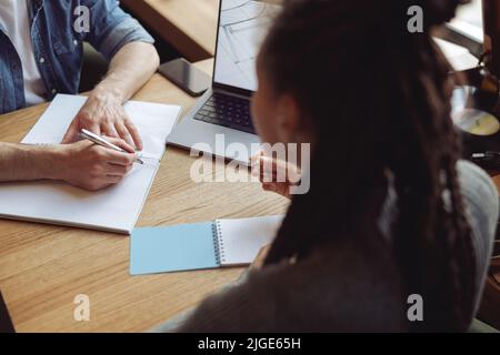 Weibliche und männliche Hände auf dem Tisch mit Notizbüchern und Stiften, die Notizen machen. Brainstorming-Konzept. Stockfoto