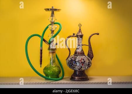 Shisha Shisha mit Glaskolben und Metallschale mit farbigem Rauch auf gelbem Hintergrund. Traditioneller östlicher Urlaub zur Entspannung Stockfoto