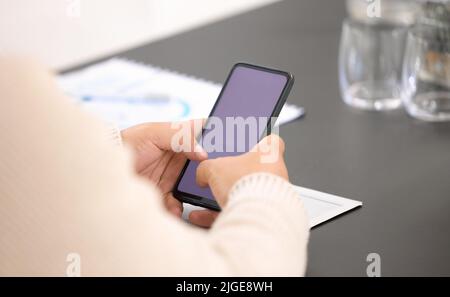 Einige Business-Updates werden überprüft. Nahaufnahme eines nicht erkennbaren Geschäftsmannes, der ein Mobiltelefon mit leerem Bildschirm in einem Büro benutzt. Stockfoto