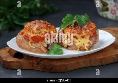 Hähnchenschenkel mit Tomaten und Käse auf einem Teller auf einem Holzbrett angeordnet, Nahaufnahme Stockfoto