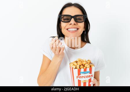 Porträt einer fröhlichen jungen Frau, die 3D Gläser beim Essen von Popcorn trägt, weißer Hintergrund Stockfoto