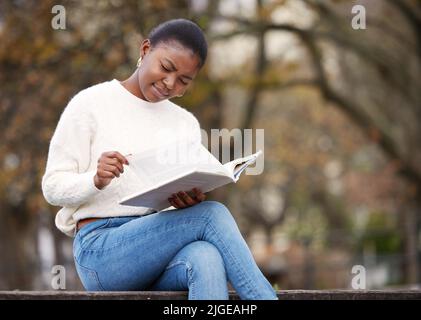 Warum machen sie es so kompliziert: Eine junge Frau, die unglücklich aussieht, während sie draußen auf dem Campus ein Buch liest. Stockfoto