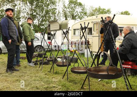 Drei Männer schauen auf einen Stand, der traditionelle Töpfe und Pfannen verkauft, Appleby Horse Fair, Appleby in Westmorland, Cumbria Stockfoto