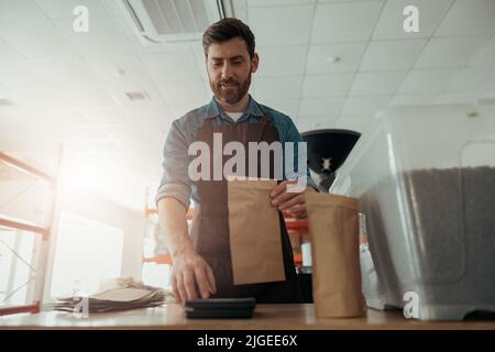Uniformierte Arbeiter verpackt geröstete Kaffeebohnen in Verpackungen zum Verkauf Stockfoto